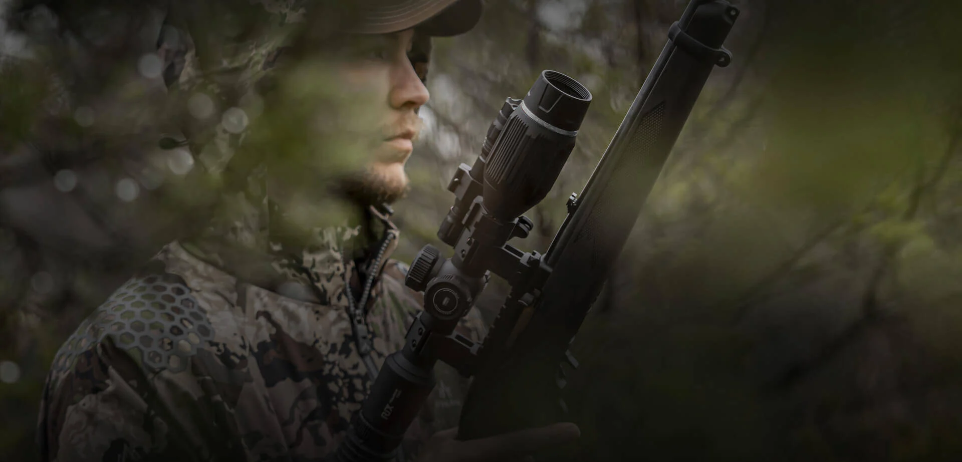 The hunter is holding a gun equipped with a night vision scope.